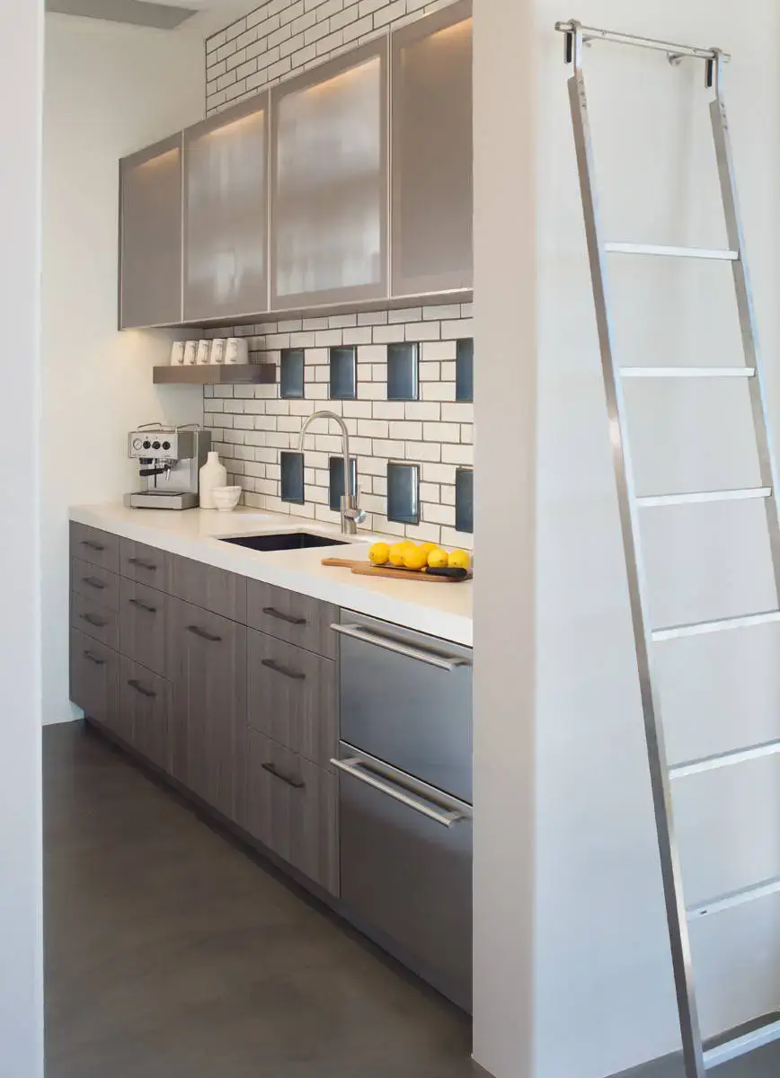Modern luxury European kitchen with sleek cabinets, stainless steel fixtures, and a minimalist design. Features include a coffee machine, decorative backsplash, and a ladder for high storage access. Ideal for contemporary home interiors.