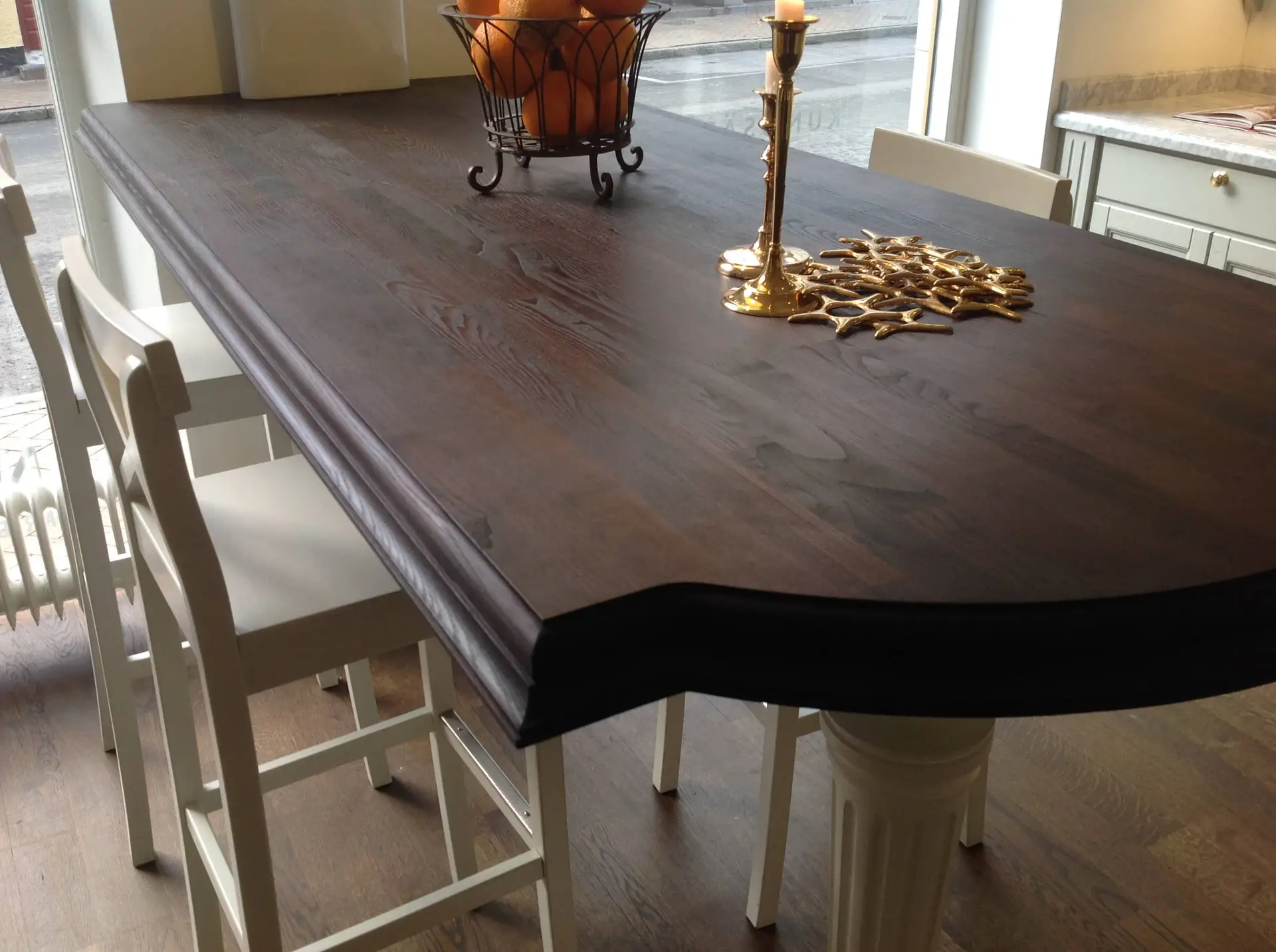 Elegant dark wooden dining table with modern white chairs, featuring a decorative centerpiece with oranges and a gold candle holder, set in a luxurious room.