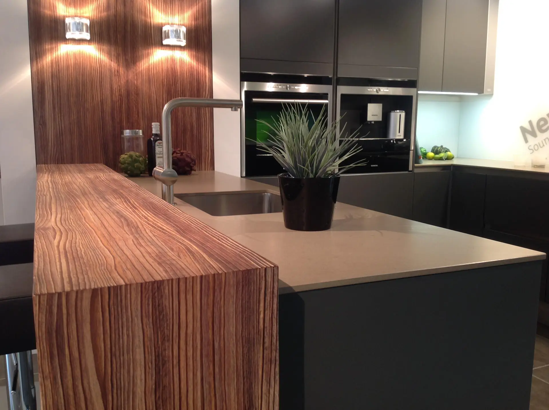 Modern kitchen design featuring custom cabinetry, sleek black cabinets, and a wood-textured island. Includes integrated appliances, a stainless steel sink, and a decorative potted plant for an elegant and functional space.