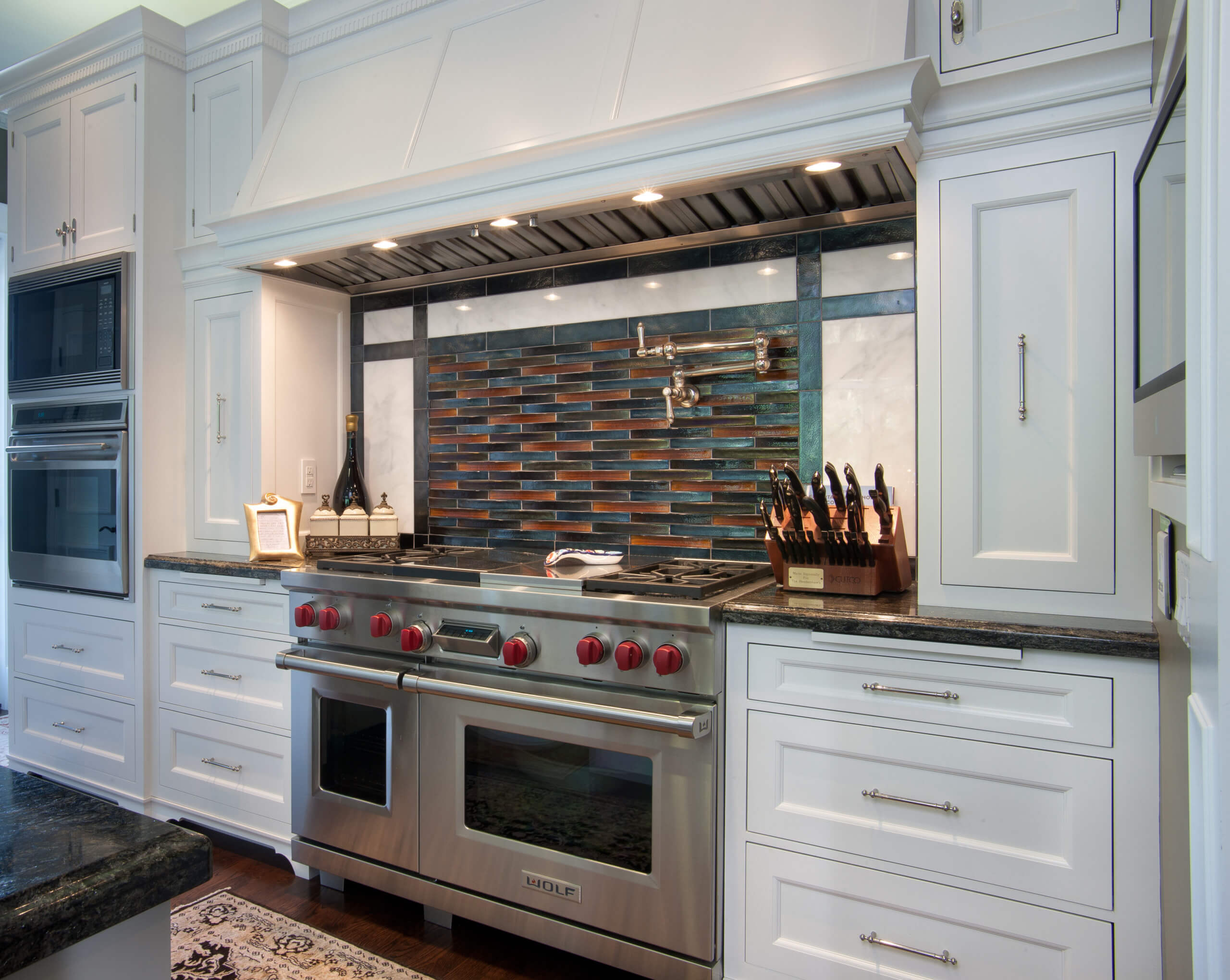 Elegant custom kitchen with a vintage style in San Diego, featuring white cabinetry, a stainless steel stove with red knobs, a colorful tile backsplash, and a knife block on the counter.