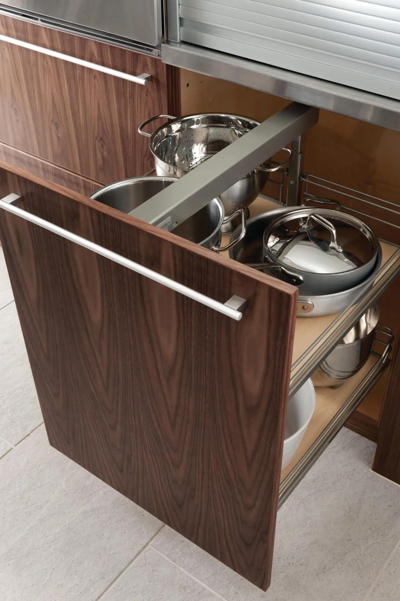 Pull-out kitchen cabinet with dark wood finish showcasing stainless steel pots and pans, exemplifying luxury kitchen design and transitional cabinetry ideas.