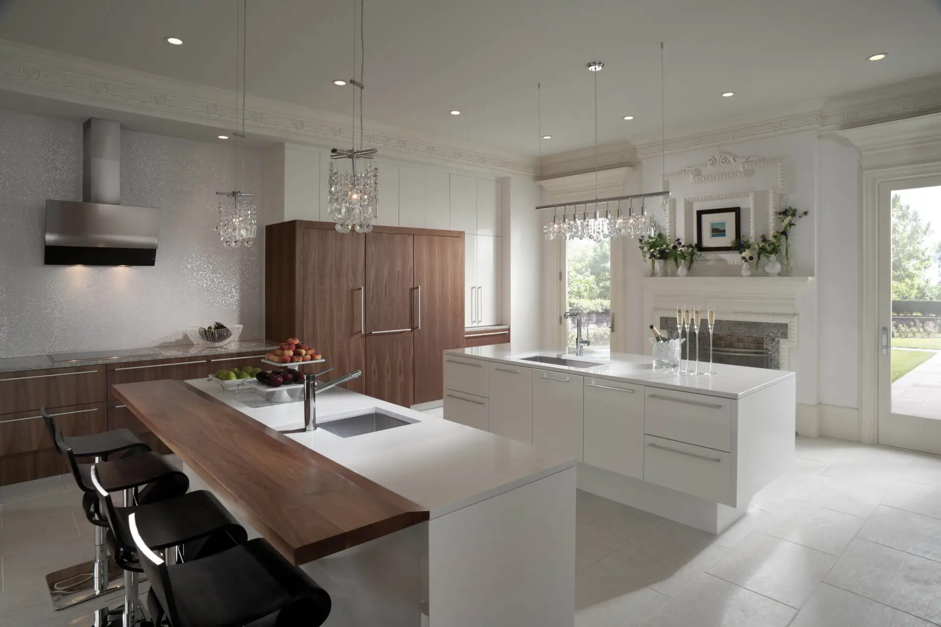 Spacious luxury kitchen with transitional cabinetry, featuring a large island with a wooden countertop extension, modern bar stools, crystal chandeliers, and stainless steel appliances. The design combines white and wooden cabinets, offering a contemporary yet classic aesthetic.