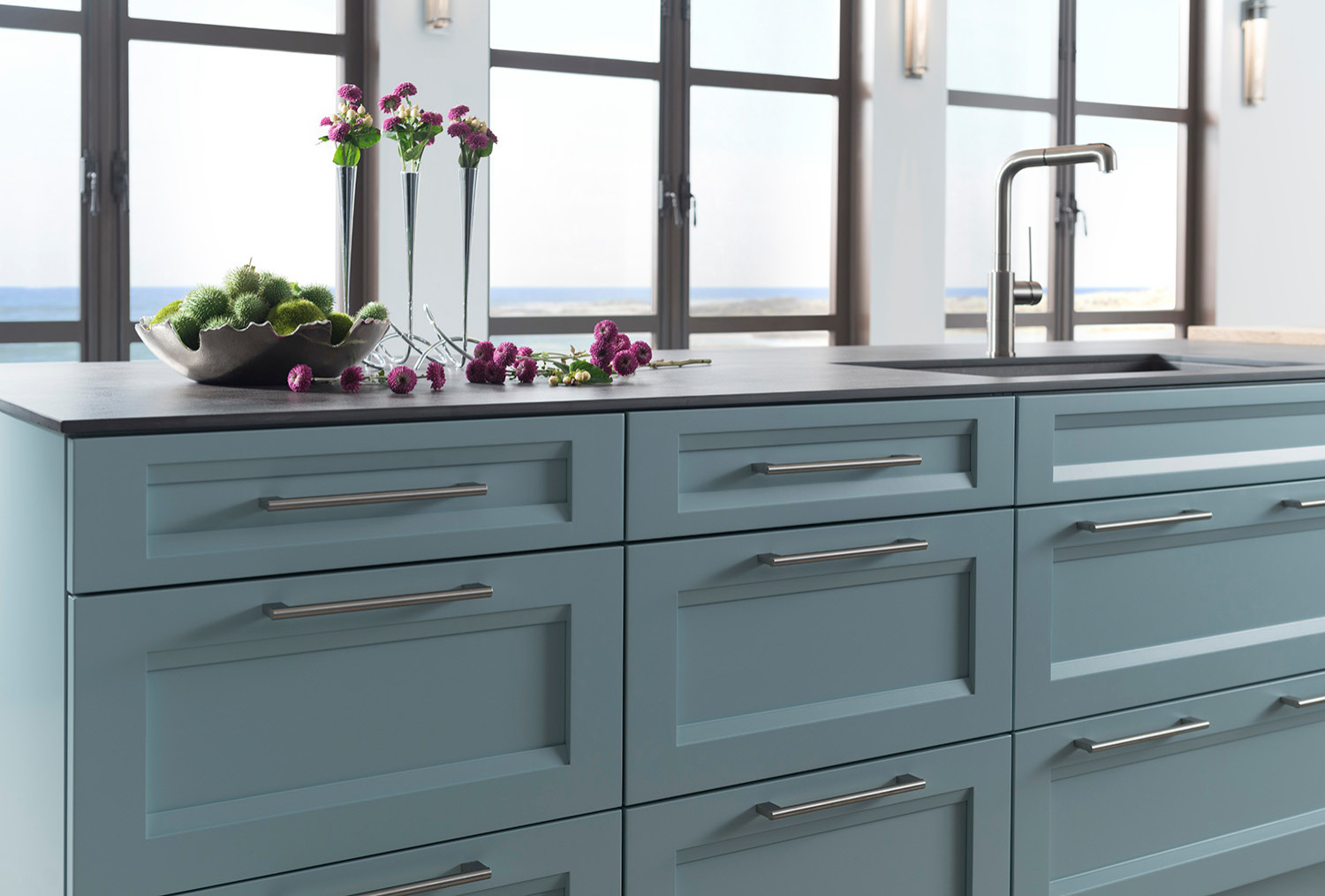 Custom light blue kitchen cabinetry with stainless steel handles, featuring an elegant countertop with purple flowers, located in a San Diego home with ocean views.