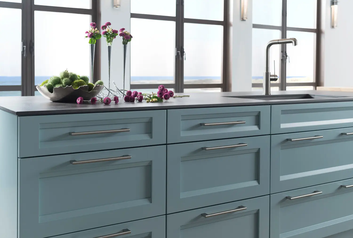 Custom light blue kitchen cabinetry with stainless steel handles, featuring an elegant countertop with purple flowers, located in a San Diego home with ocean views.