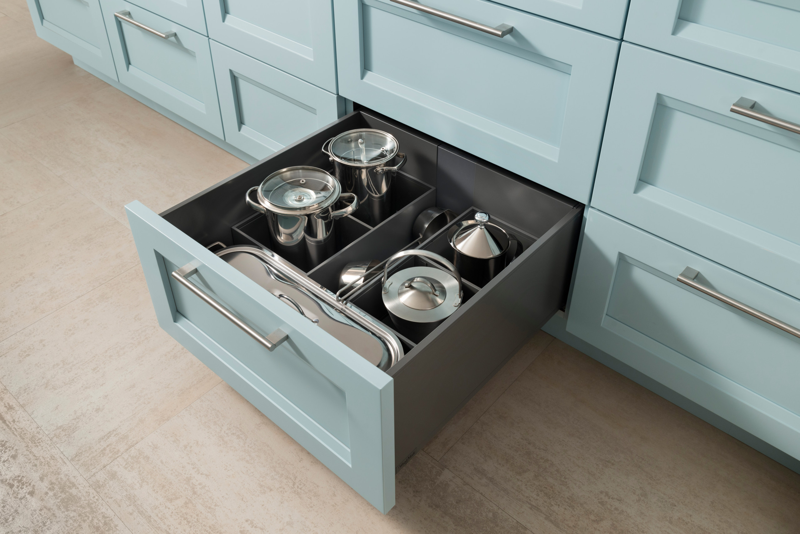 Modern light blue kitchen cabinets with open drawer displaying organized stainless steel cookware, showcasing expert custom cabinetry in San Diego.