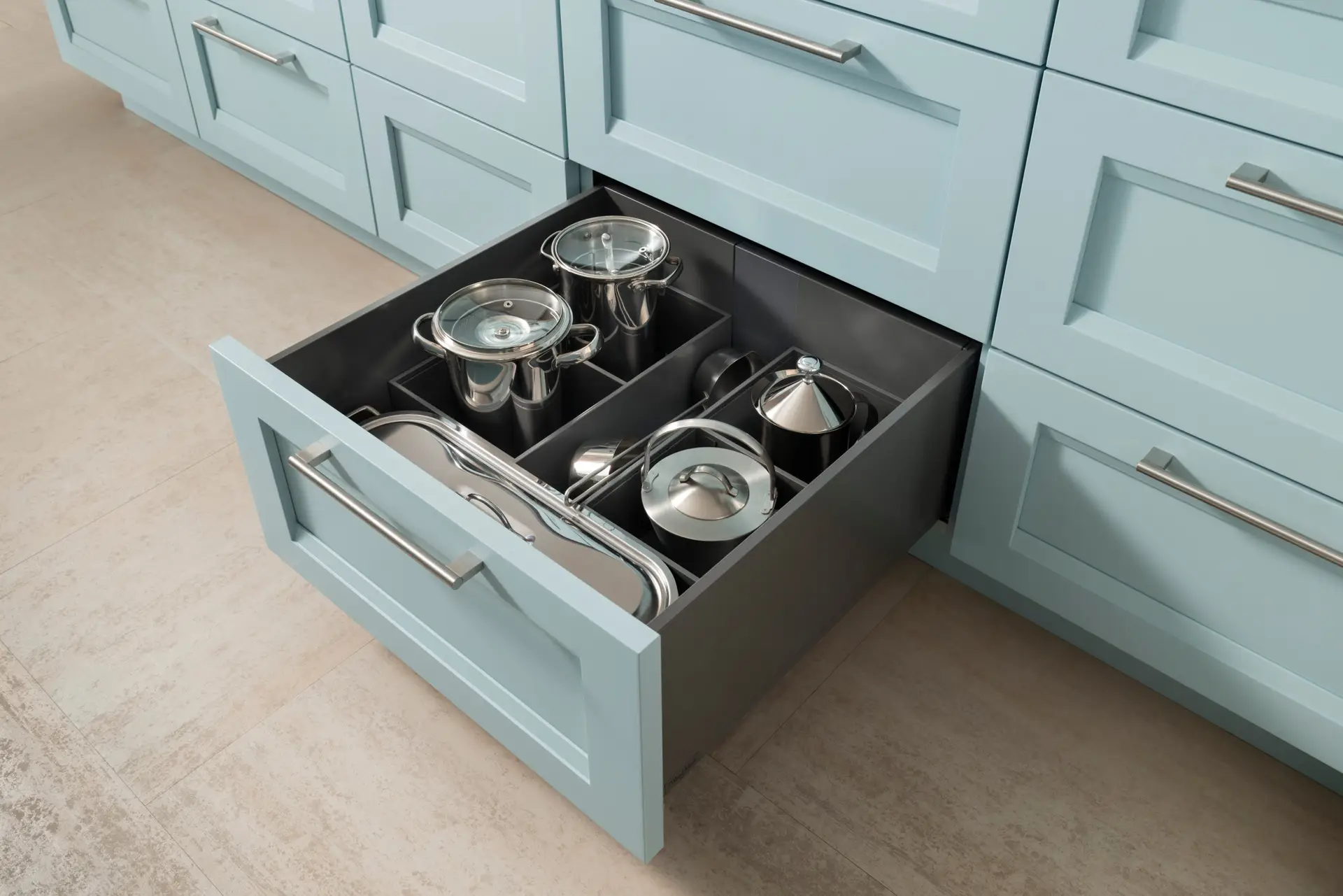 Modern light blue kitchen cabinets with open drawer displaying organized stainless steel cookware, showcasing expert custom cabinetry in San Diego.