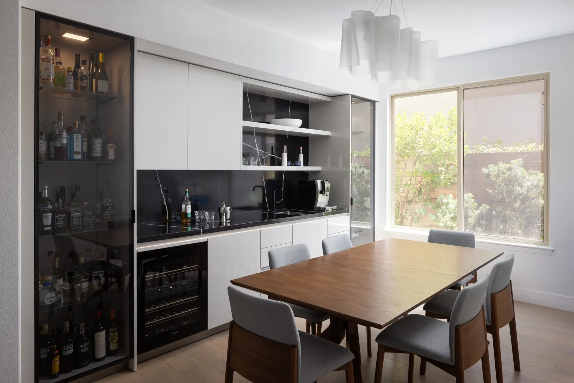 Custom home bar with smoked glass display cabinet, black stone countertop and wine refrigerator by Inplace Studio