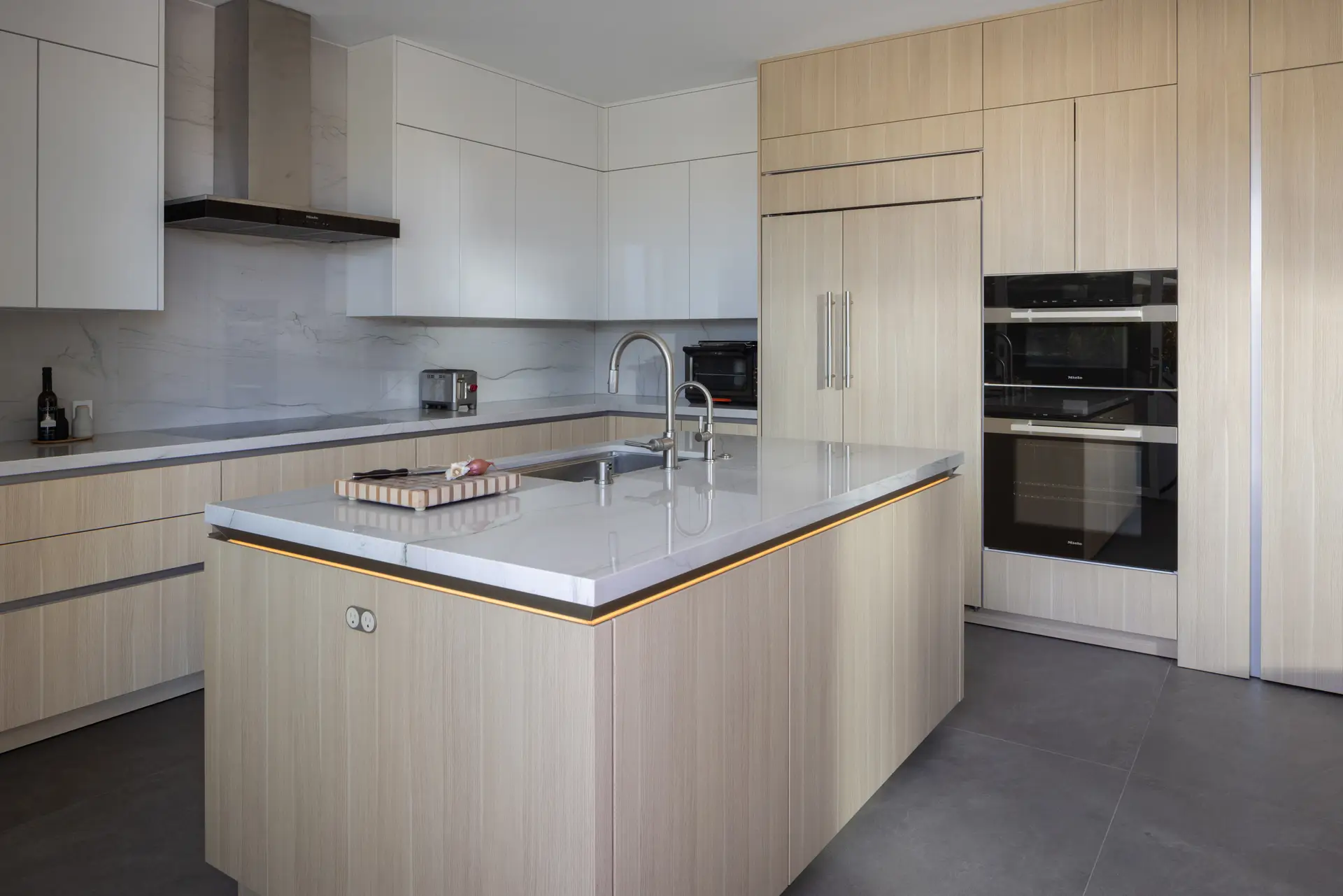 Kitchen island with stone countertop, light oak paneling and under-counter LED lighting by Inplace Studio