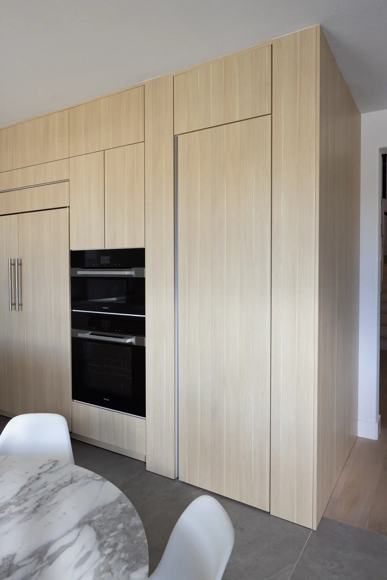 Floor-to-ceiling light oak tall cabinets with integrated Miele appliances by Inplace Studio