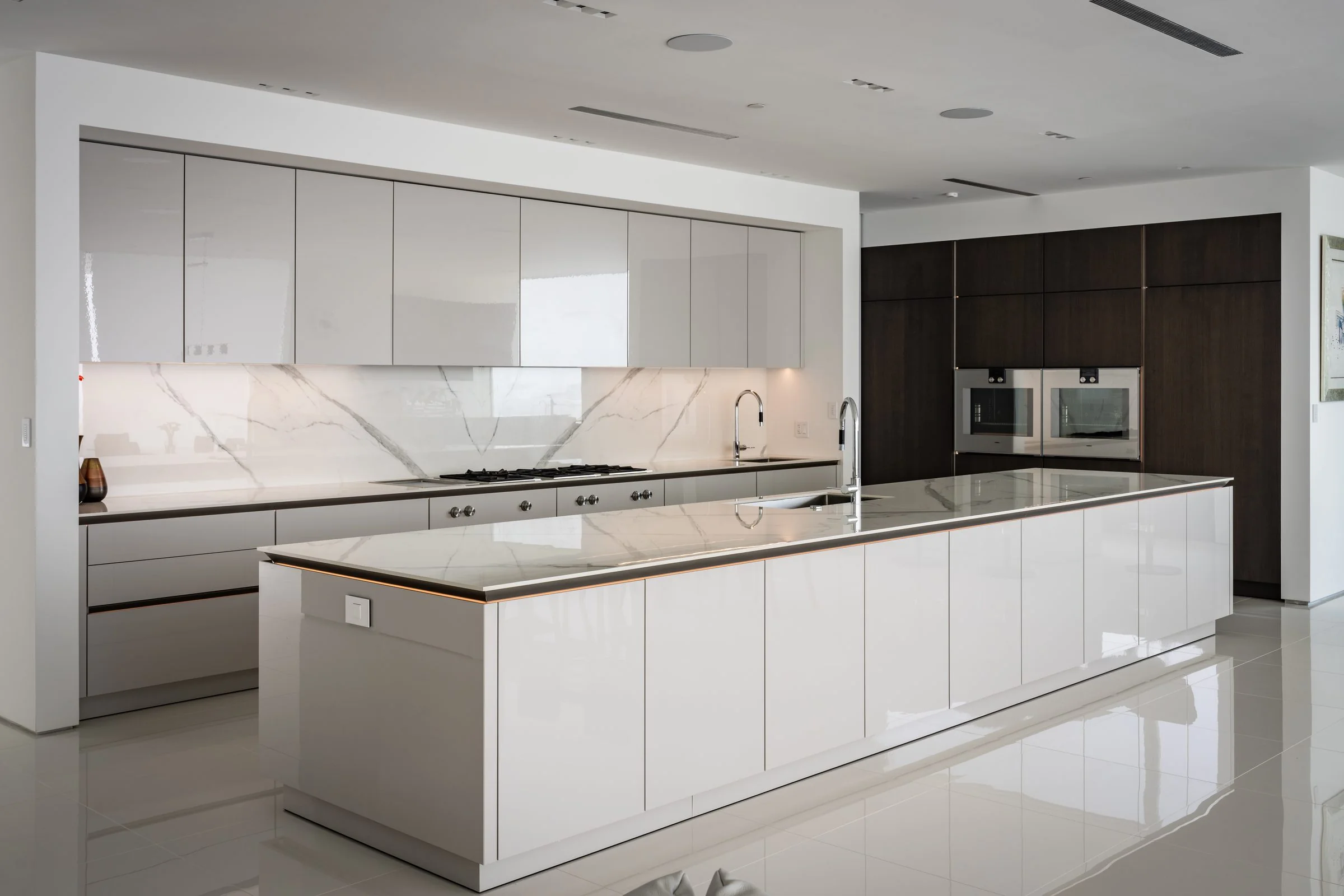 SieMatic kitchen in San Diego with white high-gloss island, marble backsplash and dark wood tall cabinets
