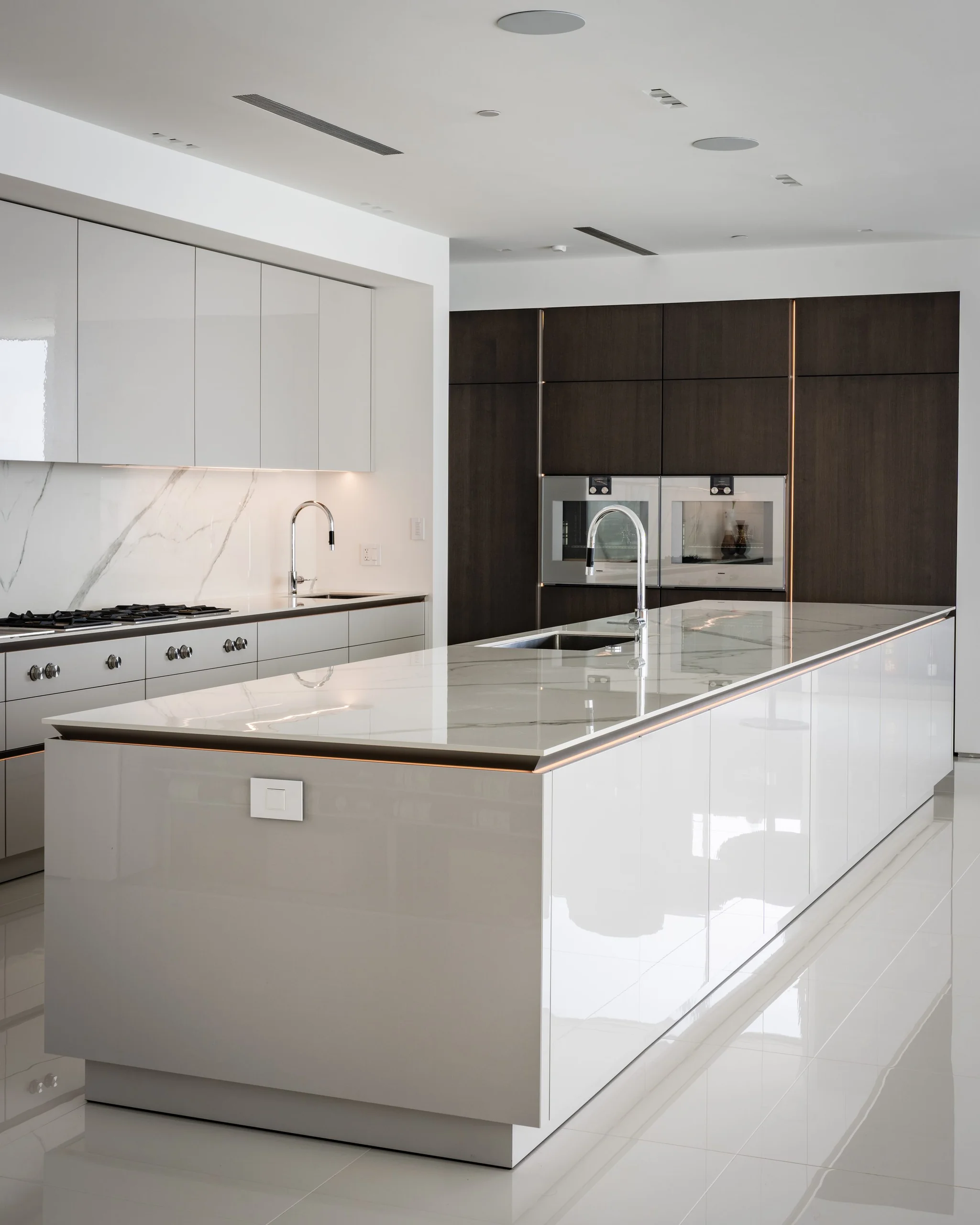 White lacquer SieMatic island with quartz top and built-in wall ovens in a modern San Diego kitchen