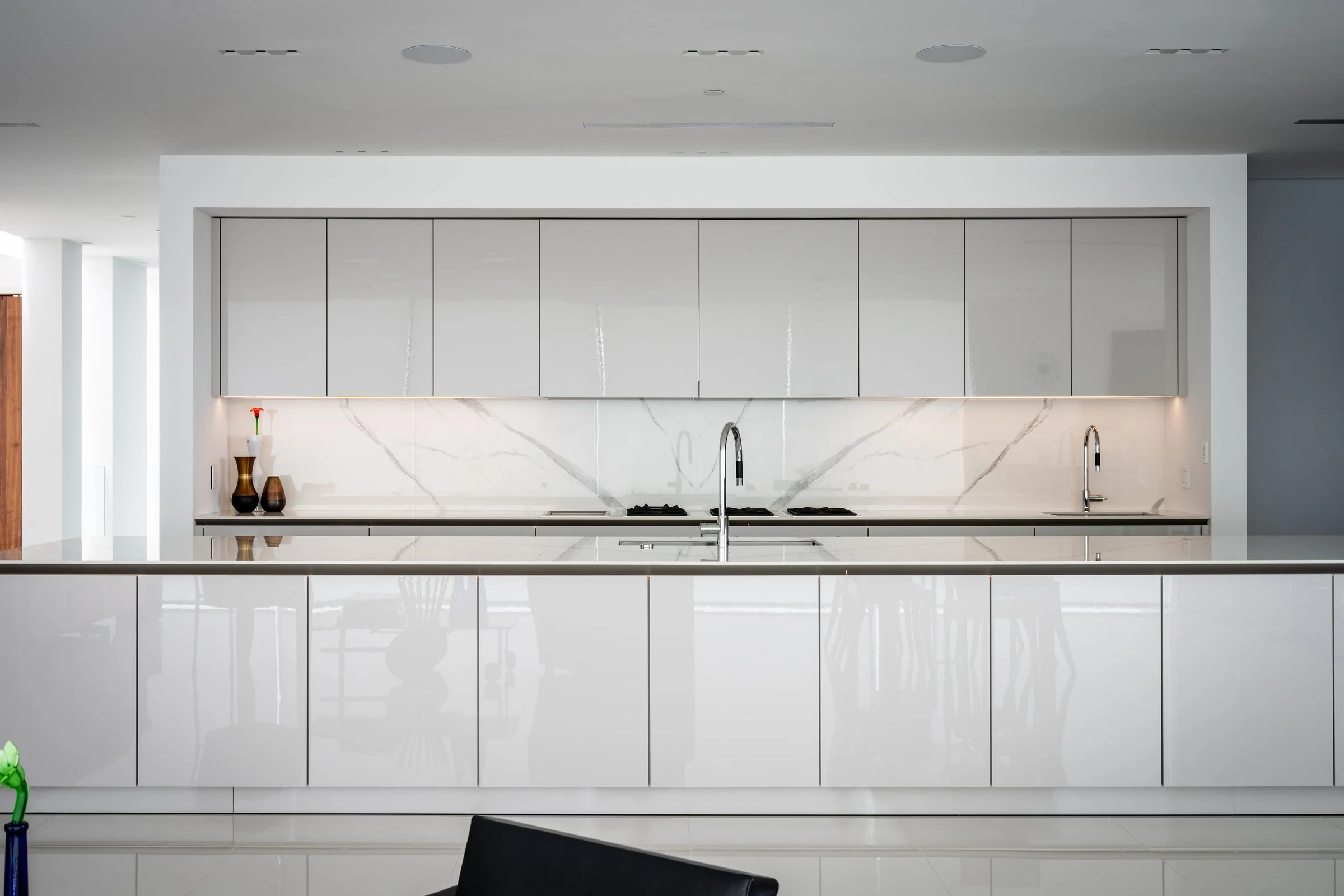 Handleless white SieMatic wall cabinets above a marble-look backsplash and long white island