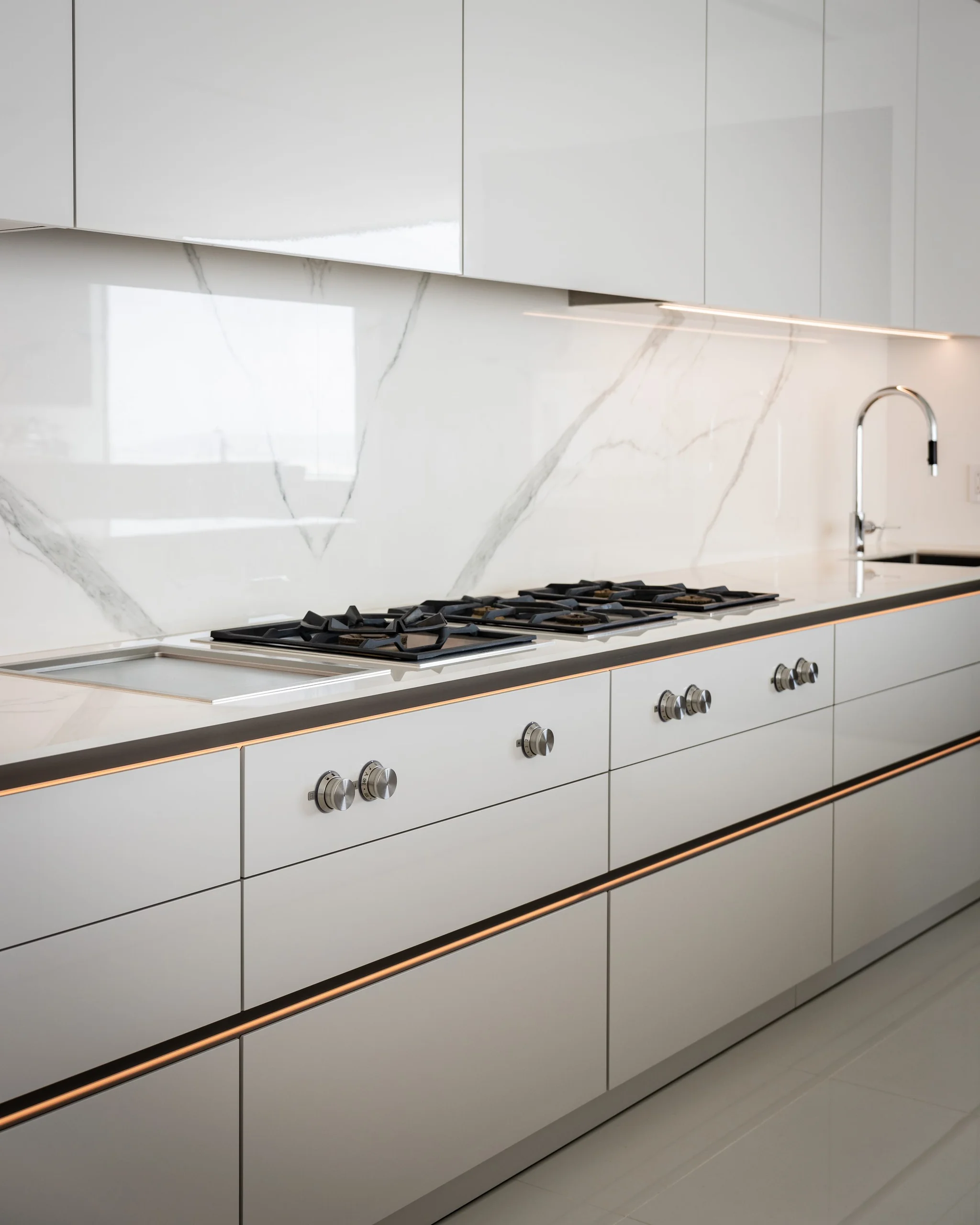 Close-up of gas cooktop and white SieMatic drawers with bronze grip-channel detail