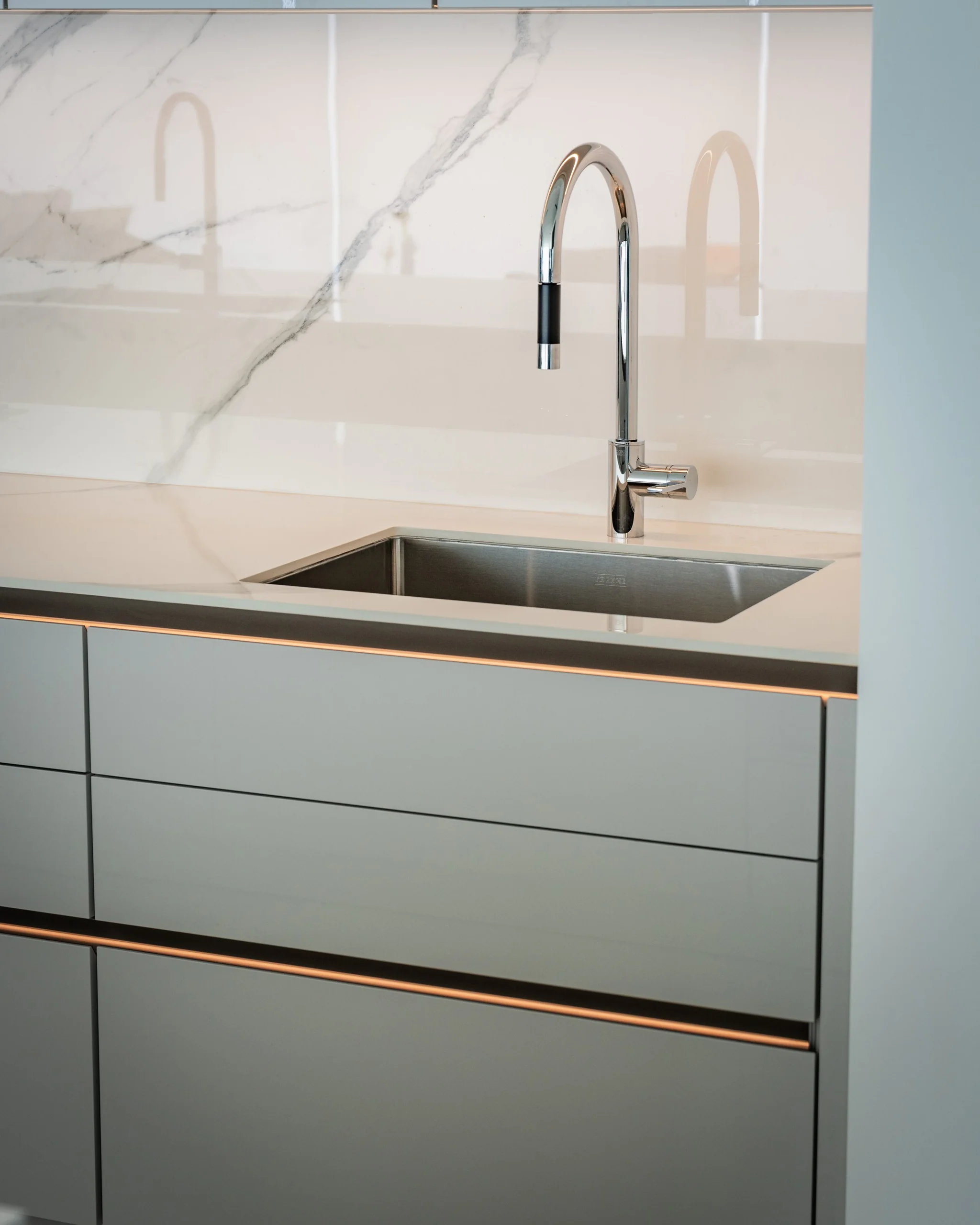 Pull-down faucet over undermount sink with white SieMatic cabinet fronts and bronze trim