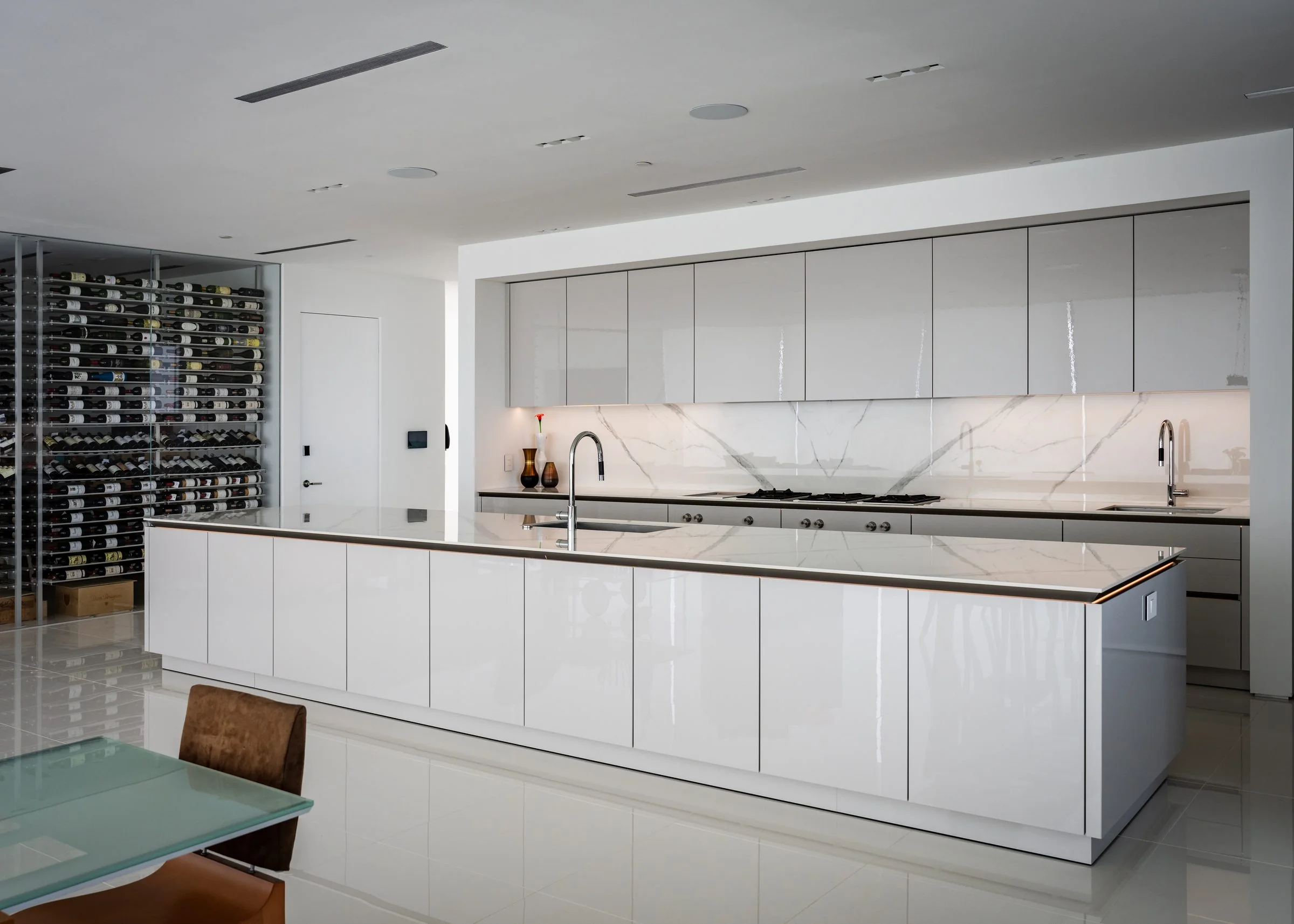 Open-plan San Diego kitchen with long white island, glass dining table and walk-in wine display