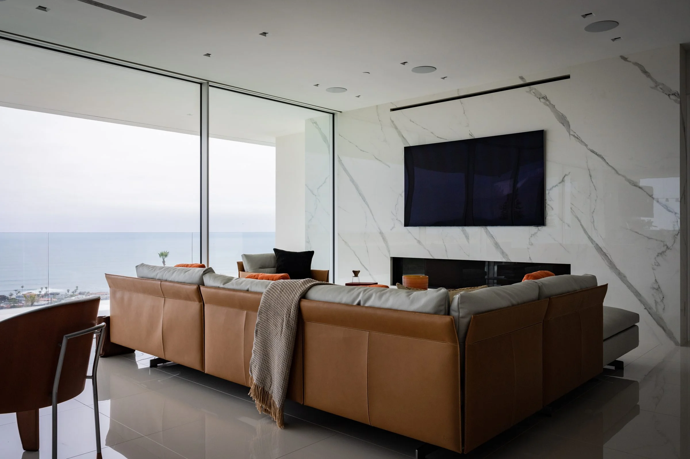 Living room with cognac leather sectional, marble feature wall and ocean view