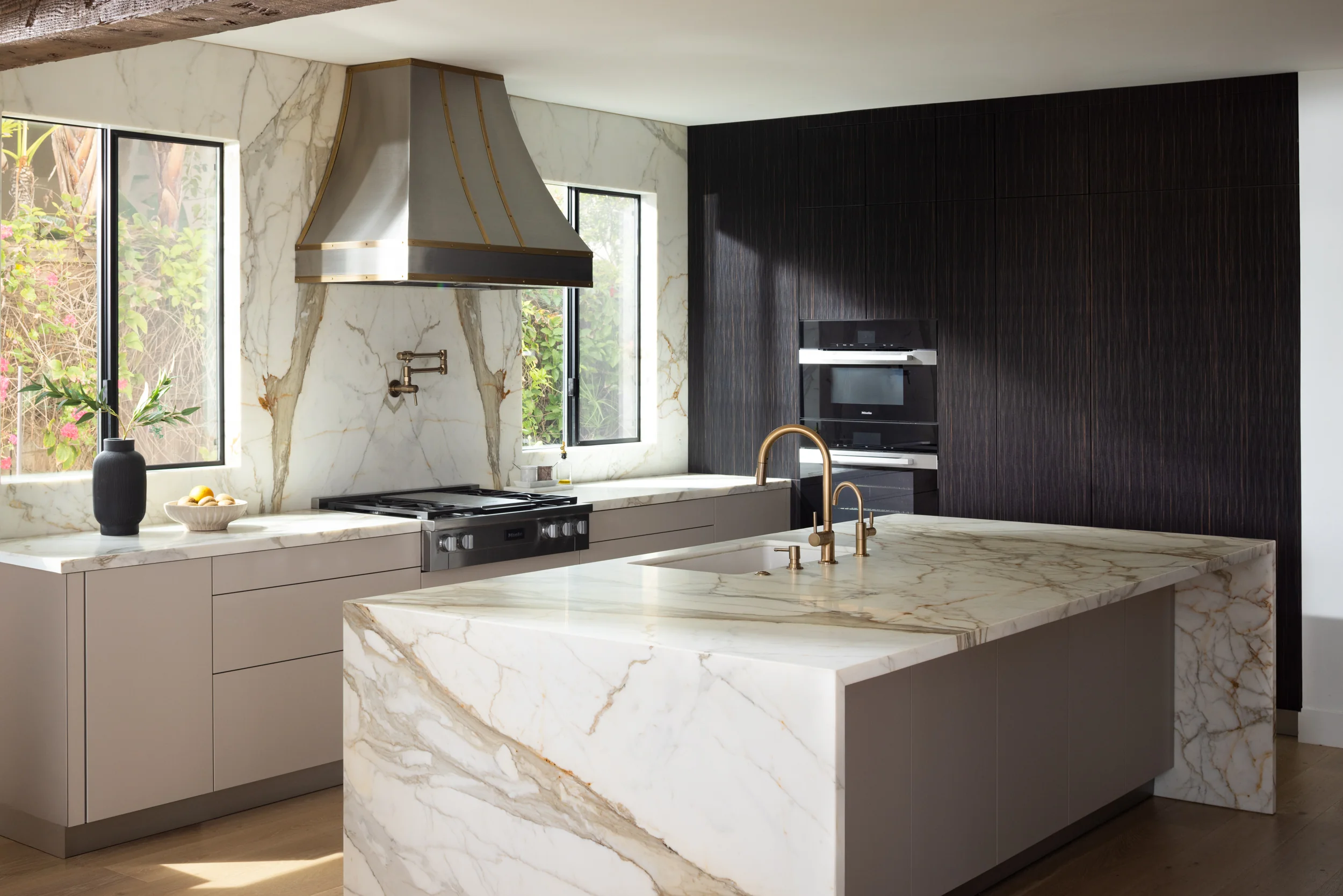 Modern kitchen with a Calacatta marble waterfall island, stainless and brass range hood, and dark wood cabinetry