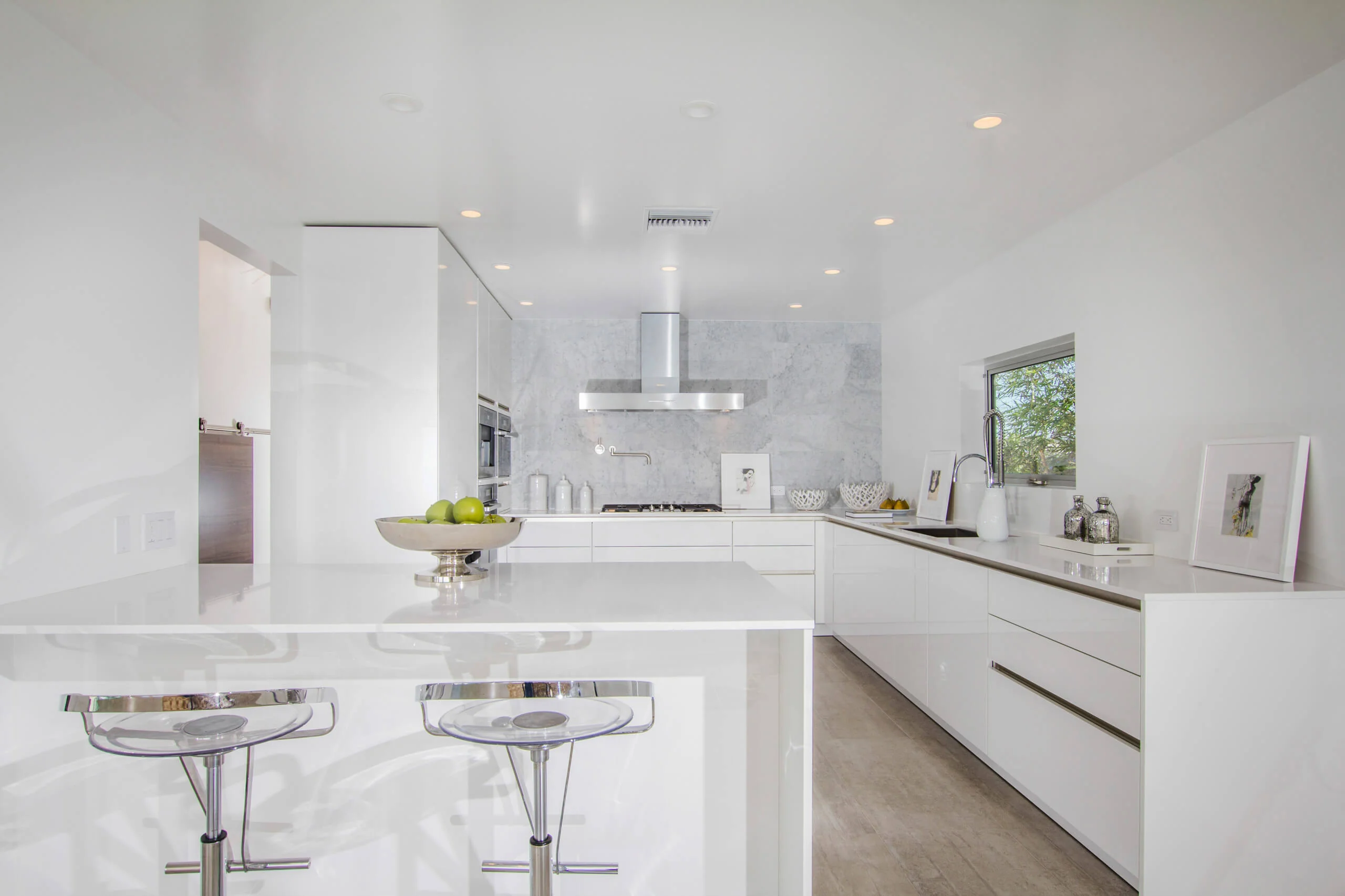 Modern kitchen with sleek custom white cabinets, island with bar stools, and stainless steel appliances in Encinitas