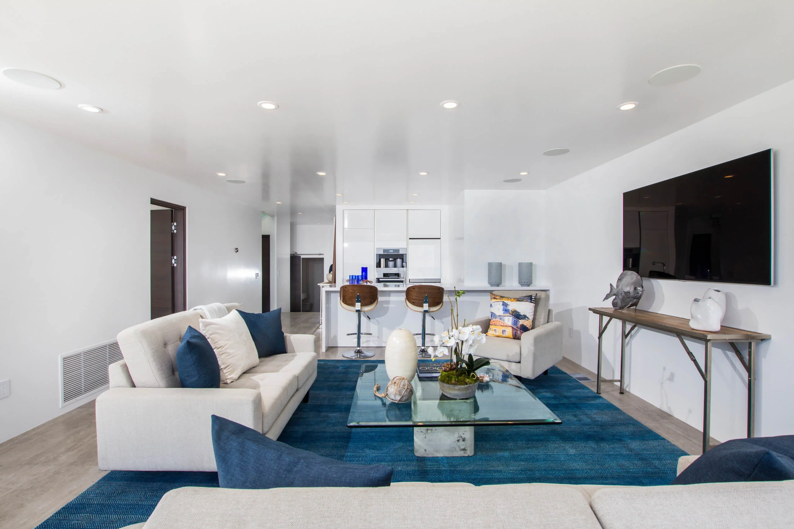 Modern living room with white custom cabinets in Encinitas, featuring a sleek design with a blue rug, glass coffee table