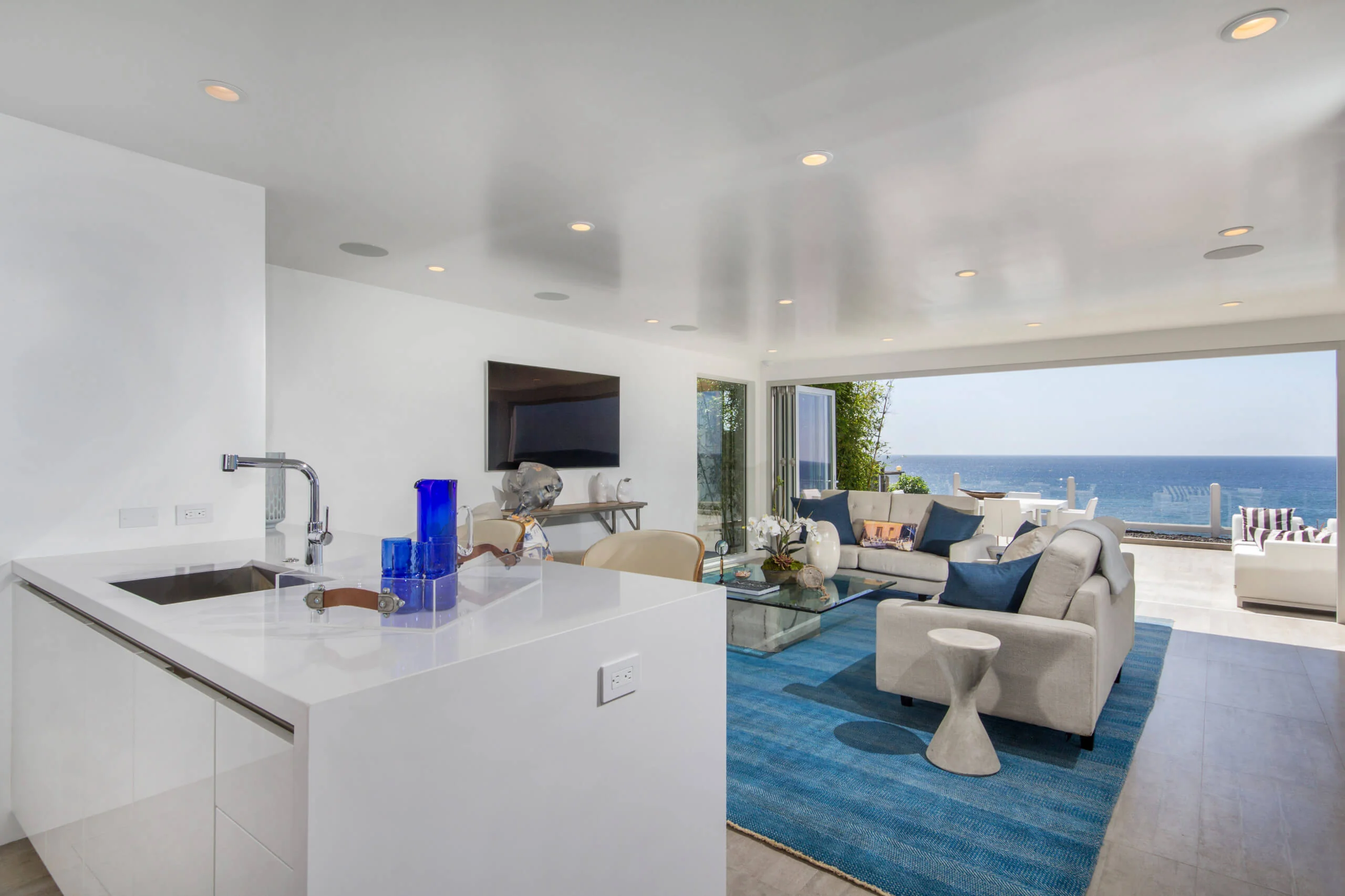 Modern open-plan living room with ocean view, featuring sleek white cabinetry, contemporary furniture