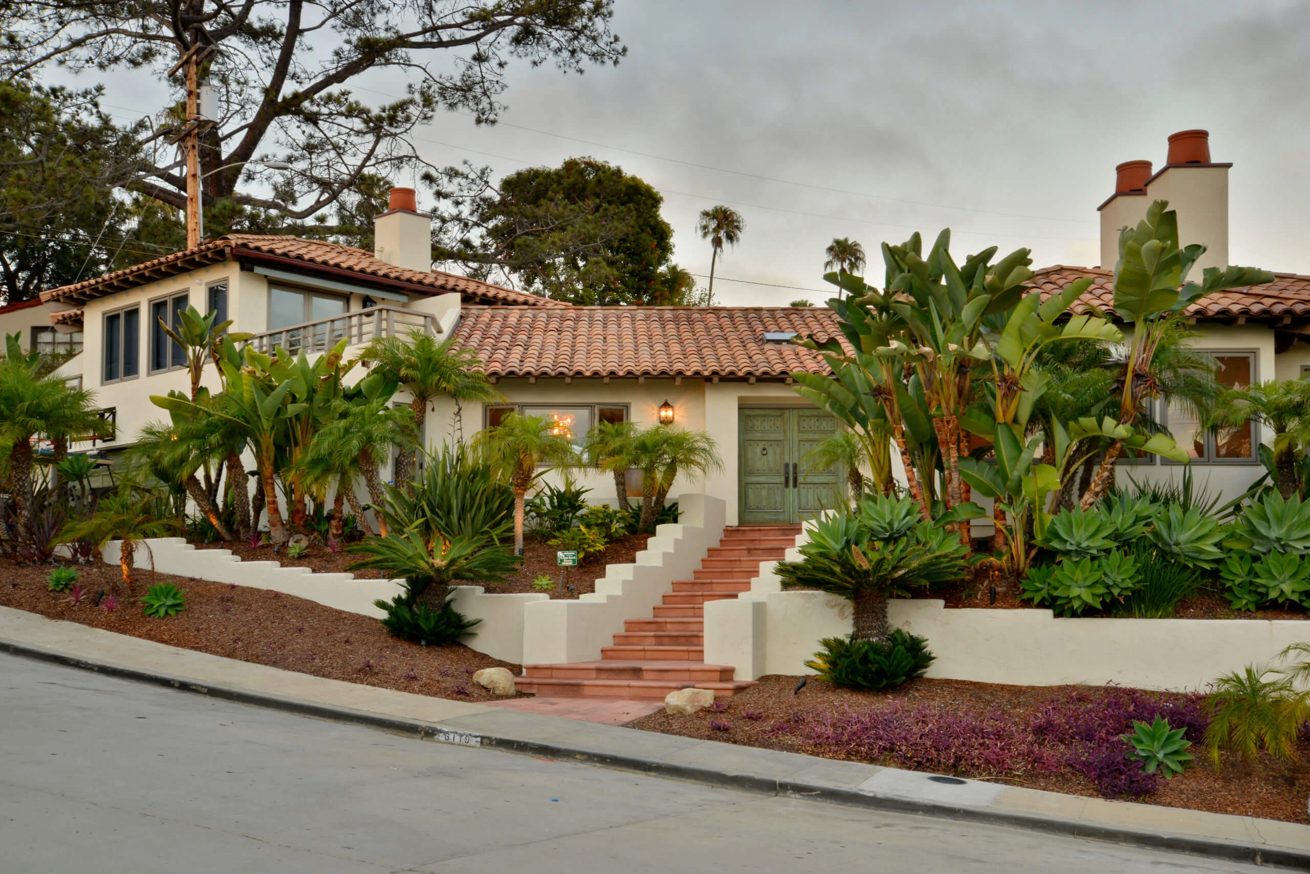 Spanish-style home featuring a red-tiled roof and rich green landscaping