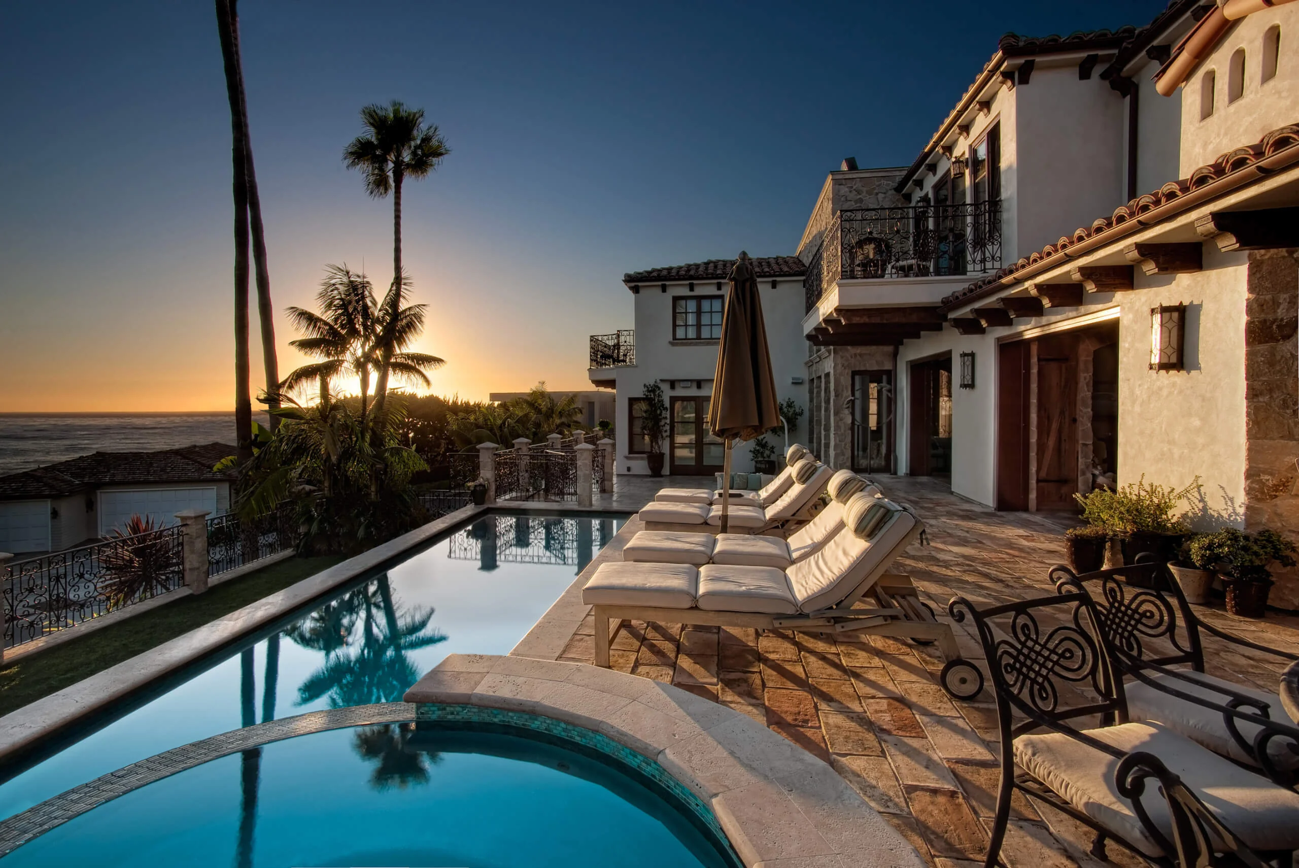 Luxurious seaside villa with elegant outdoor patio furniture, swimming pool, and ocean view at sunset